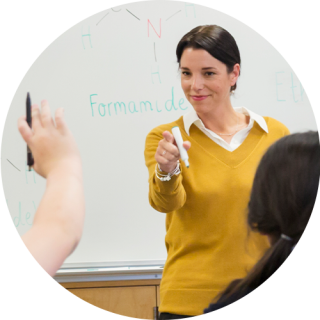 Teacher in a collared shirt holding a whiteboard marker, pointing next to the board